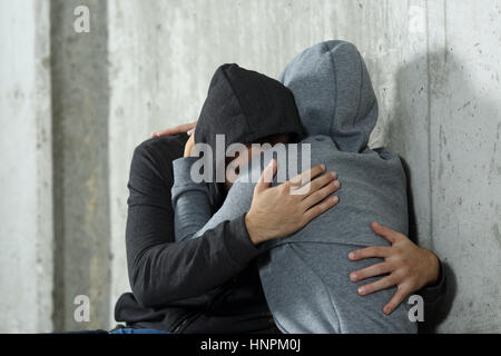 Triste paio di adolescenti durante la riconciliazione dopo argomento seduto sul pavimento e appoggiato a una parete Foto Stock