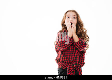 Sorpreso curly bambina in plaid shirt coperto aprì la bocca con le mani su sfondo bianco Foto Stock