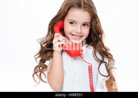 Allegro carino bambina parlando al telefono rosso su sfondo bianco Foto Stock