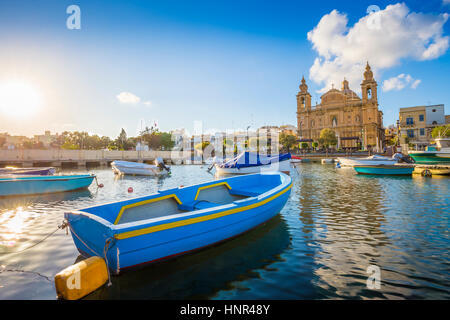 Msida, Malta - Blu tradizionale barca da pesca con il famoso Msida Chiesa Parrocchiale a sfondo su un giorno di estate con cielo blu e nuvole Foto Stock