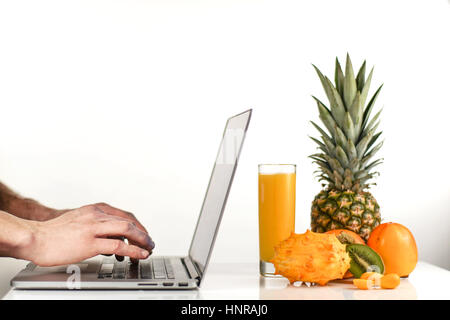 Persona che lavora alla scrivania con laptop moderno computer vicino a frutta fresca su sfondo bianco Foto Stock