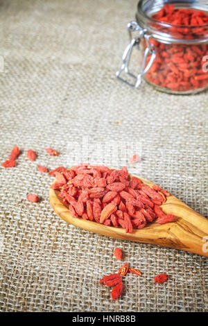Essiccati goji bacche su un cucchiaio di legno, biancheria sfondo, il fuoco selettivo. Goji bacche sono una fonte eccellente di antiossidanti. Foto Stock