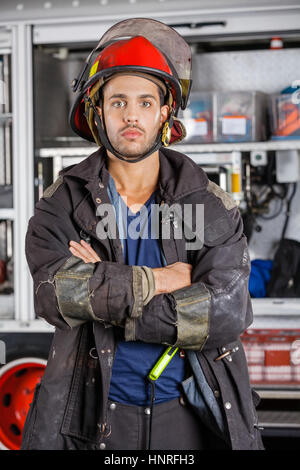 Grave vigile del fuoco in piedi con le braccia incrociate contro firetruck Foto Stock