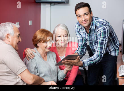 Il tutor guidare gli studenti senior per utilizzare digitale compressa in aula Foto Stock