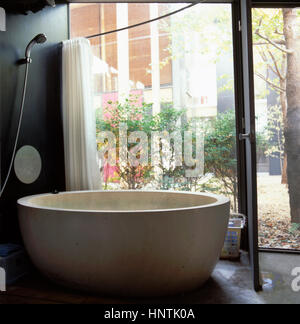Interno di una contemporanea bagno con una porta di fronte ad un giardino privato con una grande vasca da bagno in casa giapponese a Tokyo in Giappone Foto Stock