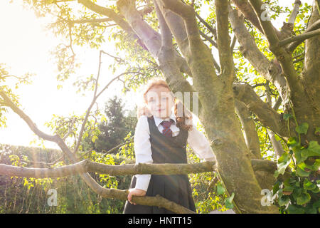 Una bambina di arrampicarsi su un albero nella sua scuola uniforme. Foto Stock