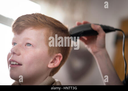 Un ragazzo avente il suo taglio di capelli con clippers e forbici. Foto Stock