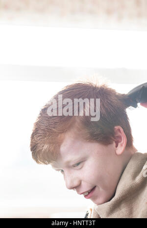 Un ragazzo avente il suo taglio di capelli con clippers e forbici. Foto Stock