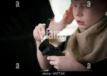 Un ragazzo avente il suo taglio di capelli con clippers e forbici. Foto Stock