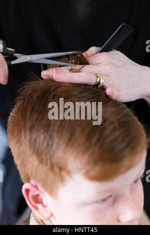 Un ragazzo avente il suo taglio di capelli con clippers e forbici. Foto Stock