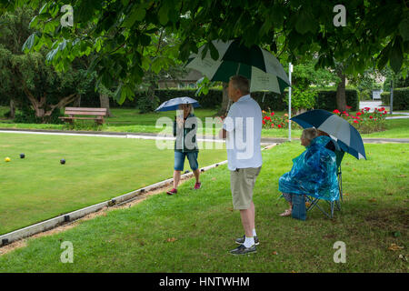 Gli spettatori, con ombrelloni, riparo dalla pioggia in una corona verde partita a bowling - village bowling green, Burley in Wharfedale, West Yorkshire, GB. Foto Stock