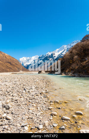 Langtang valley ad alta quota con flusso di fiume glaciale acqua dalla montagna himalayana di gamma e snow-capped Gangchenpo picco in background in Nepa Foto Stock