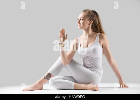 Giovane donna attraente in Ardha Matsyendrasana pongono, grigio studio Foto Stock