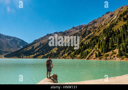 Uomo caucasico permanente sulla roccia vicino al lago di montagna Foto Stock