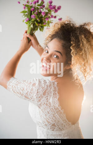 Razza mista donna che indossa abiti da sposa tossing bouquet Foto Stock