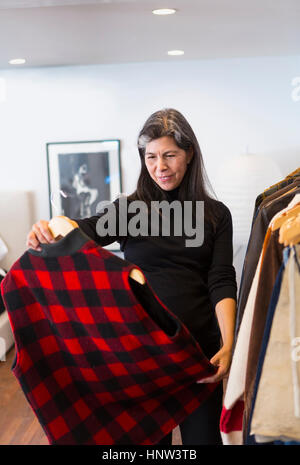 Donna ispanica esaminando plaid gilet in negozio Foto Stock