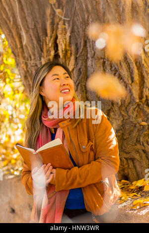 Sorridente donna asiatica la lettura di libro in autunno Foto Stock