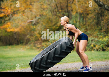 La donna caucasica il sollevamento di un carico pesante pneumatico in posizione di parcheggio Foto Stock
