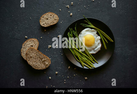 Pane e briciole vicino a piastra con uovo fritto e asparagi Foto Stock