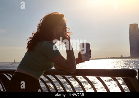 Giovane turista femminile appoggiata contro la ringhiera sul lungomare con caffè, Manhattan, New York, Stati Uniti d'America Foto Stock