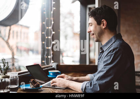 Uomo al lavoro su computer portatile presso il cafe Foto Stock