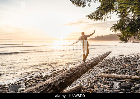 Uomo in equilibrio su driftwood log sulla spiaggia di Juan de Fuca Parco Provinciale, Isola di Vancouver, British Columbia, Canada Foto Stock