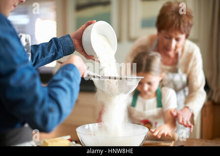 Donna Senior e nipoti setacciare la farina per i cookie Foto Stock