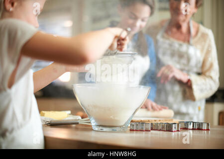 Donna Senior e nipoti setacciare la farina per albero di Natale i cookie Foto Stock