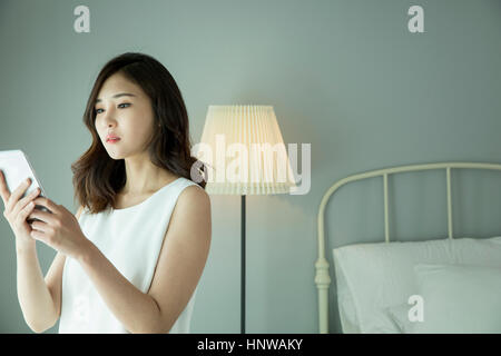 Giovane donna utilizza lo smartphone in camera da letto Foto Stock