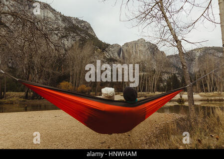 Vista posteriore del giovane reclinate in rosso amaca a guardare il paesaggio, Yosemite National Park, California, Stati Uniti d'America Foto Stock