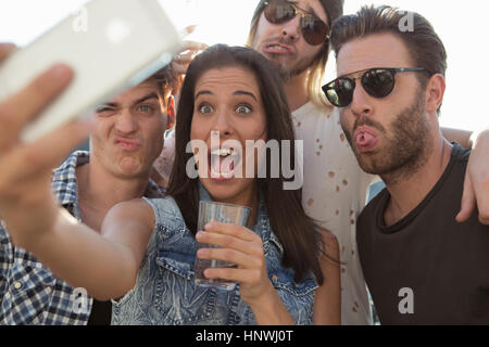 Giovani amici adulti tirando facce per selfie presso la terrazza sul tetto delle parti Foto Stock