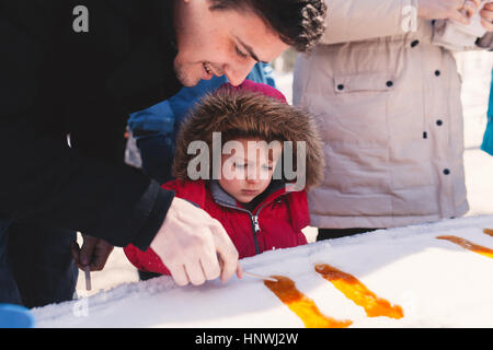 La ragazza di cappa pelliccia con padre rendendo per lecca-lecca in snow ice Foto Stock