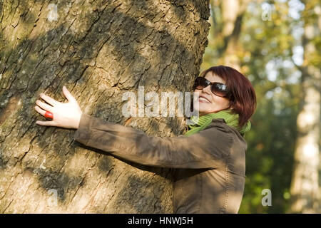 Modello di rilascio, Junge Frau im Herbst umarmt einen Baumstamm - giovane donna in autunno abbracciando un tronco di albero Foto Stock