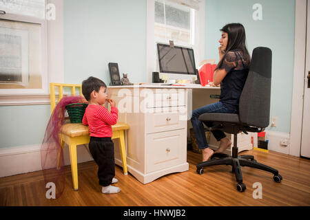 Bimbi maschio mangiare cookie mentre la madre utilizzando laptop Foto Stock