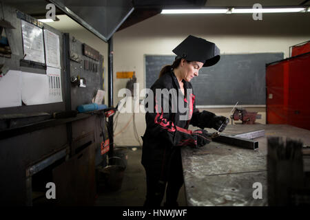 Femmina esaminando metalsmith asta metallica al banco di officina Foto Stock