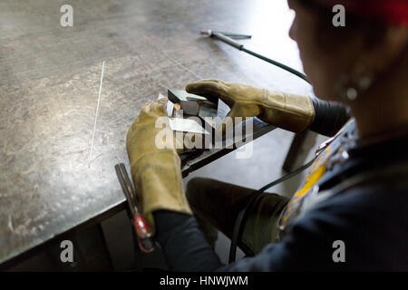 Sulla spalla vista metalsmith femmina allineamento di metallo sul banco di officina Foto Stock