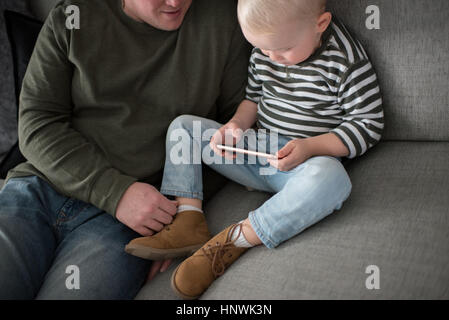 Padre e figlio seduti sul divano, figlio guardando smartphone Foto Stock