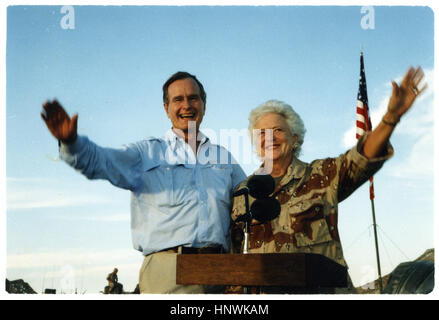 Il presidente George Bush e la First Lady Barbara Bush come onda che stare nella parte posteriore di un veicolo durante una visita ad un accampamento del deserto. Il presidente e sua moglie stanno pagando la Giornata del Ringraziamento visite alle truppe degli Stati Uniti che sono in Arabia Saudita per Operazione Desert Shield. 1990 Foto Stock