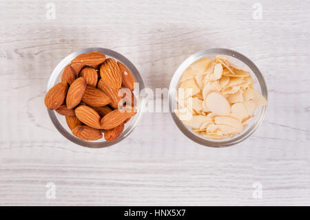 I dadi di mandorla e fette di trucioli in piccoli piatti in vetro su un tavolo di legno Foto Stock