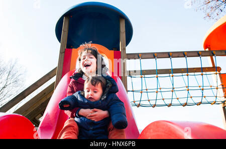 Ragazzo e baby fratello lo scorrimento verso il basso il parco giochi slitta Foto Stock