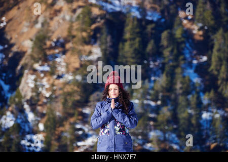 Donna in knit hat a praticare yoga e meditazione di fronte Montagna innevata Foto Stock