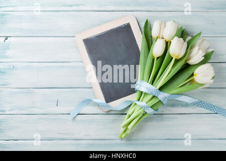 Bianco bouquet di tulipani e lavagna su sfondo di legno. Con spazio per i messaggi di saluto Foto Stock