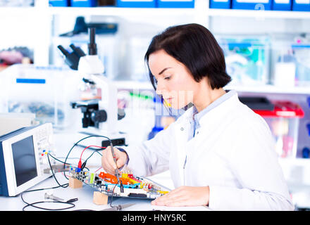 Ingegnere di lavoro con i circuiti. Una donna ingegnere circuiti saldature seduti ad un tavolo. Microchip fabbrica di produzione. Il processo tecnologico. Assemblaggio Foto Stock