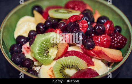 Una sana insalata di frutta in una ciotola verde con mirtilli e kiwi, banana, plumb Foto Stock