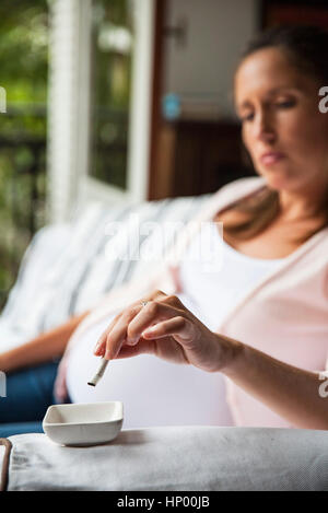 Donna incinta mettendo fuori di sigaretta in un portacenere Foto Stock