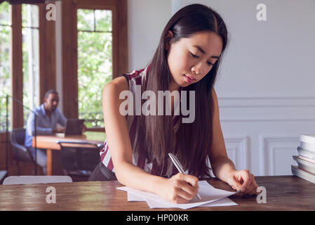 Giovane donna scrittura su carta mentre l uomo orologi lei in background Foto Stock