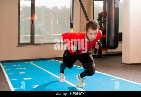 Ricci bianco barbuto uomo sportivo esercitando con cinghie di fitness in palestra Foto Stock