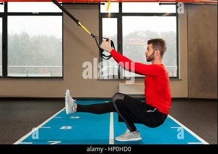 Ricci bianco barbuto uomo sportivo esercitando con cinghie di fitness in palestra Foto Stock