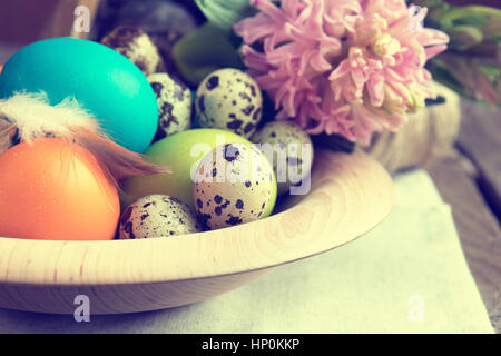 Pasqua colorata e uova di quaglia in vaso di legno con giacinto rosa scuro su un tavolo di legno. Tonica foto. Foto Stock