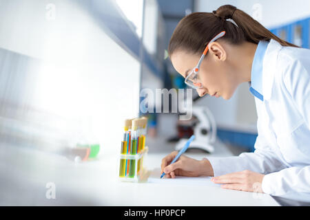 Scienziato a scrivere i risultati del test durante il lavoro in laboratorio Foto Stock